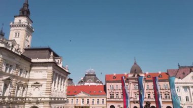 View a breathtaking panorama of NoviSad center, highlighting the stunning buildings and vibrant atmosphere under a clear blue sky. Experience the charm of this historic location.