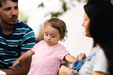 A family scene showcasing parents interacting with their young child, expressing love and care. The photo captures a warm and candid moment in an outdoor setting.