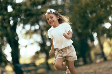 Joyful young child running actively outdoors in a sunny park, showcasing a happy and carefree moment in nature among lush greenery.