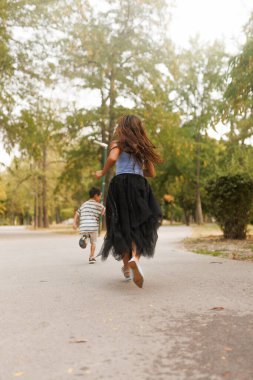 Joyous children enjoying a leisurely run down a park pathway on a sunny afternoon, surrounded by vibrant greenery.