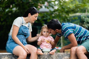 A young family enjoys a relaxing moment together outdoors, sitting on a bench amidst the greenery.