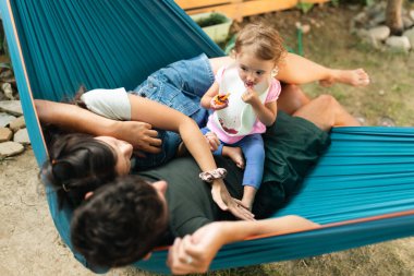 A family of three enjoying their day in a cozy hammock outdoors. Their bond and joy reflect the happiness of togetherness and a shared moment of relaxation.