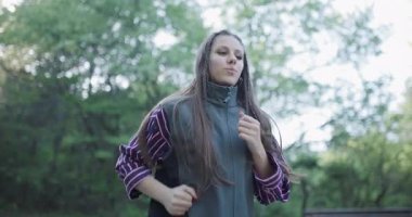 A girl jogs along a forest trail, surrounded by vibrant greenery and sunlight filtering through the trees. She wears a green vest and a striped shirt, exuding energy and joy.