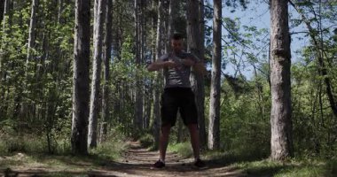 A person is exercising in a beautiful forest setting, showcasing various fitness movements among tall trees and greenery.