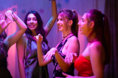 A group of women celebrating and dancing, creating joyful moments in a festive setting. The scene is filled with positive energy, illuminated by colorful lighting, emphasizing the fun and celebratory