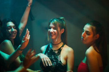 Friends having fun dancing and socializing in a dimly lit indoor environment, smiling and enjoying.