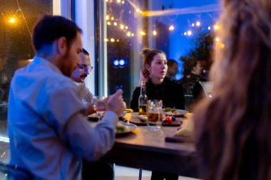 A lively scene of friends dining together in a cozy restaurant setting, engaging in conversations and enjoying delicious meals during a festive evening filled with warm, inviting lights and ambiance.