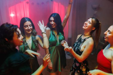 A group of young women smiling and dancing enthusiastically together, creating a cheerful and lively atmosphere, with colorful lighting enhancing the fun mood of the celebration.