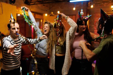 Group of joyful friends enjoying a festive celebration indoors with party hats, decorative items, and laughter together.