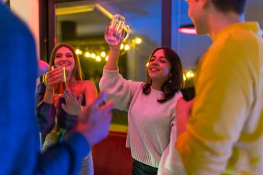 A lively group of friends enjoying beverages and celebrating in a cozy indoor setting during night. The atmosphere is joyful and warm, highlighting companionship, cheer, positive social interactions.