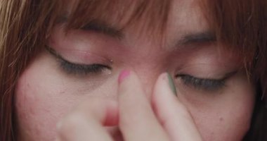A detailed close-up image of a young Asian woman focusing on her eyes as she gently touches her face, capturing a moment of introspection.