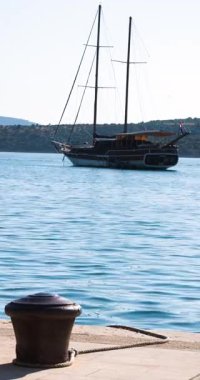 A tranquil view of NS sea ship harbour V showcases a sailboat anchored close to the dock. The clear waters reflect the bright sun and surrounding hills, creating a serene atmosphere.