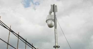 A surveillance camera captures cloud movements above a construction site on an overcast afternoon, providing a view of the surrounding area and weather conditions.