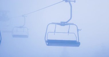 Empty chairlift moving through thick fog on Kopaonik mountain. Winter sports and bad weather conditions abstract.