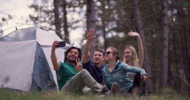 Bir grup genç yetişkin ormanda kamp yapıyor, selfie çekiyor ve beşlik çakıyor, arkadaşlığı somutlaştırıyor ve dışarıda eğleniyor..