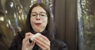 Dışarıda yemek yiyen genç bir kadın peçeteyle ağzını siliyor, diş tellerini ve gözlüklerini gösteriyor..