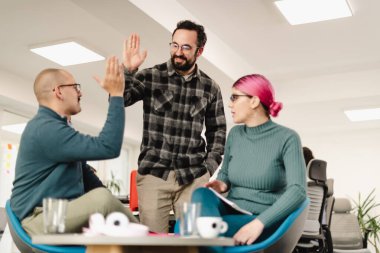 Three businesspeople are engaging in a lively discussion in a contemporary office space. They share ideas while enjoying a collaborative atmosphere. The room is bright and modern.