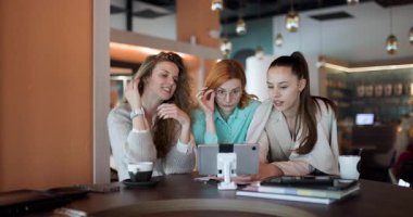 Three women discuss important business strategies in a contemporary cafe setting, sharing ideas and collaborating on their projects while enjoying their beverages.
