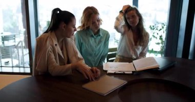 Three businesswomen engage in a meaningful discussion around a large table in a contemporary office. They collaborate on strategies while reviewing important documents and sharing insights.