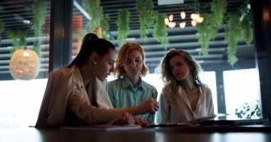 A group of businesswomen gathers in a modern workspace, actively discussing ideas, taking notes, and collaborating on projects that aim to empower women in business.