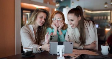Three women engage in a lively discussion while seated in a modern cafe, actively sharing insights and brainstorming new business ideas over coffee with focused expressions.