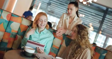In a modern cafe, three women share ideas and collaborate enthusiastically on a project while enjoying coffee. Their conversation radiates teamwork and creativity in a stylish atmosphere.
