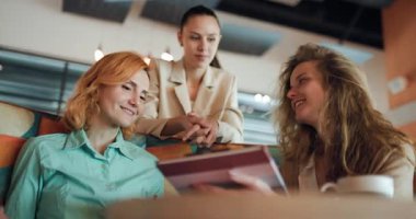 Three businesswomen engage in a productive discussion at a modern cafe, sharing insights and strategies while enjoying a collaborative environment.