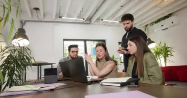 Four colleagues gather around a laptop, engrossed in a discussion. They analyze data and strategize, fostering teamwork and collaboration in the workplace.