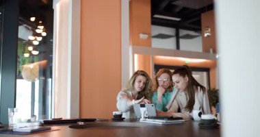 Three businesswomen engage in collaboration at a stylish workspace, discussing ideas while enjoying coffee. The environment is lively and encourages productive conversations among peers.