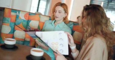Two businesswomen engage in a productive meeting at a contemporary cafe, sharing insights as they review documents and evaluate key strategies for their upcoming projects.