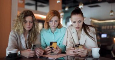 Three businesswomen in a contemporary office setting collaborate on strategy planning, focusing on their smartphones to share important insights and ideas during their meeting.