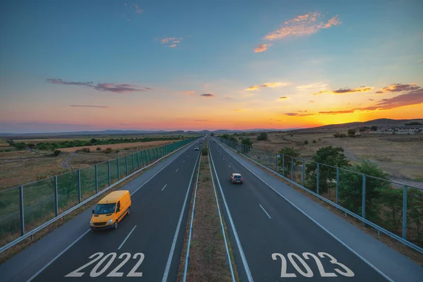Driving on open road toward new year 2023 at sunset. Aerial view of highway, driving car, van and truck. Transportation, logistic, travel concept