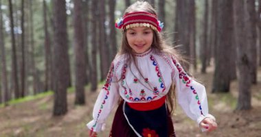 Dağlarda ormanda koşan geleneksel folklor kostümlü Bulgar kız, 4K ağır çekim videosu. Bulgaristan doğası ve halkı.