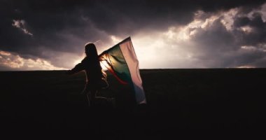 Güzel bir Bulgar kızı, genç bir kadın ve yeşil tarım sahasında uzanan bir Bulgar bayrağı. Özgürlük, güzellik, İspanya bağımsızlığı ve gurur konsepti, 4k video