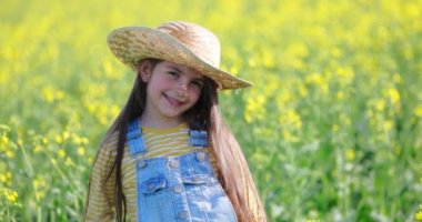 Taze bahar tarlasında hasır şapkalı ve kot pantolonlu çiftçi küçük kız yeşil bitkiler, tarım videosu 4k
