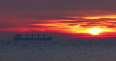 Kargo gemisi dramatik gündoğumu sırasında deniz dalgalarında yelken açıyor. Güzel okyanus ufku.