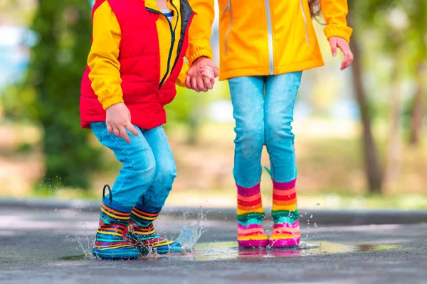幸せな子供たち女の子と男の子とともに傘とカラフルなゴムレインブーツ遊び屋外とジャンプで雨水たまり — ストック写真