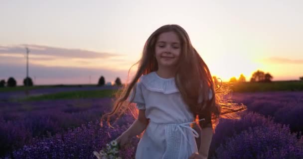 幸せな屈託のない女の子とともに美しいドレスでランニングでラベンダーフィールド行で日没 — ストック動画