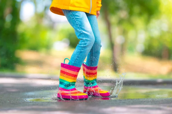 公園で雨の水たまりを飛び越えるカラフルなゴム製のレインブーツの子供の足 — ストック写真