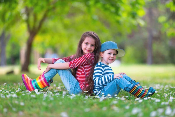 幸せな子供たち男の子と女の子で雨ゴムブーツは外で遊んで緑の公園でデイジーの花の咲くフィールド — ストック写真