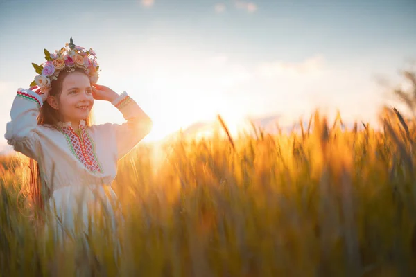 小麦畑で夕日の間に花の連句 伝統的なブルガリアの刺繍と民族の民俗衣装を持つ美しい若い女の子 — ストック写真