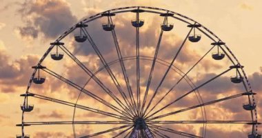 Eğlence parkında dönen dönme dolap ve gökyüzünde manzaralı günbatımı bulutları 4K sinematik video