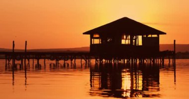 Balıkçı çadırı ve ahşap iskele üzerinde deniz gölü suyunda balık ağları olan manzaralı gün batımı.