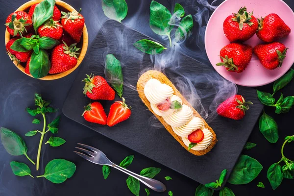 チョコレートやフルーティーなストロベリークリームや甘いイタリアのプロフィールや新鮮なジューシーなイチゴ 黒を背景にした食べ物で覆われたフランスのエクレア — ストック写真