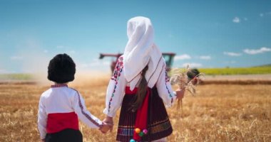 Folklor kostümlü Bulgar çocuk ve kız hasat makinesiyle altın buğday tarlasında çalışıyorlar. Bulgaristan 4K videosu