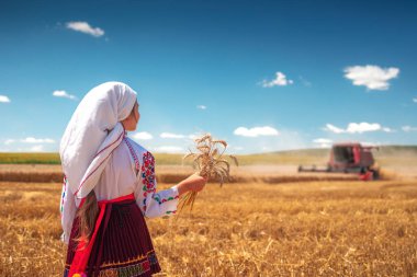 Hasat zamanı tarım buğday tarlasında geleneksel Bulgar folklor kostümlü genç kız sanayi makinesiyle birleştirildi