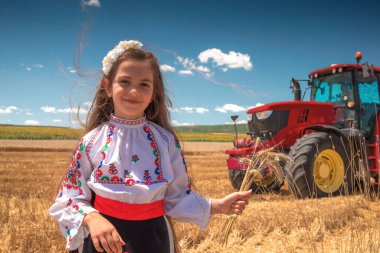Geleneksel Bulgar folklor kostümlü genç kız sanayi traktörüyle hasat zamanı tarım buğday tarlasında