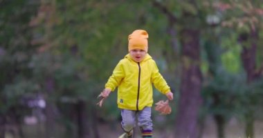 Sonbahar parkı ve renkli lastik çizmelerle sonbahar yapraklarının üzerinde koşan mutlu küçük çocuk.