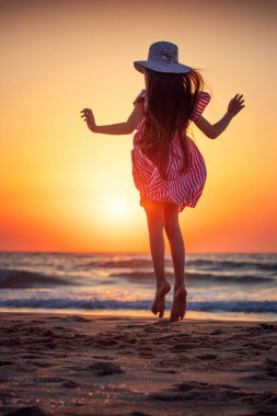 Okyanus sahili gün doğumu ve kumlu sahilde yürüyen ve dans eden mutlu küçük kız.