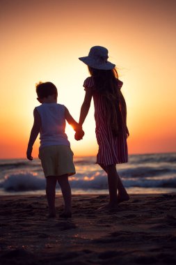 Deniz doğuyor ve kıyıda mutlu bir aile, kumsalda yürüyen kardeşler